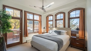 A bedroom with a large bed, a ceiling fan, and multiple windows with curtains.
