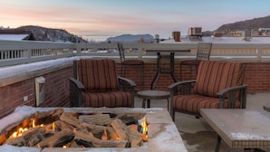 A rooftop patio with a fire pit, outdoor seating, and a view of a snowy landscape.
