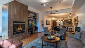 A spacious living room with a fireplace, comfortable seating, and a kitchen in the background.
