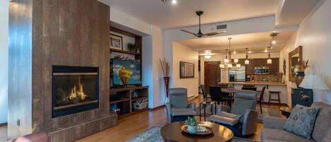 A spacious living room with a fireplace, comfortable seating, and a kitchen in the background.