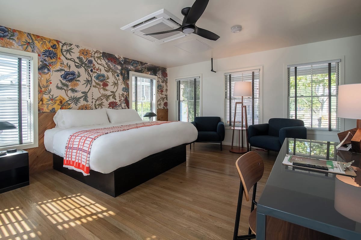 Una habitación de hotel moderna con una cama grande, dos sillones, un escritorio y un ventilador de techo.