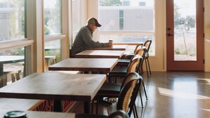 A cafe with wooden tables and chairs, large windows, and an exit door. - Talbot Commons Hotel (Taylor)