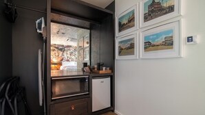 A compact kitchen with a microwave, coffee maker, and a small refrigerator. There are framed historical photos on the wall. - Talbot Commons Hotel (Taylor)