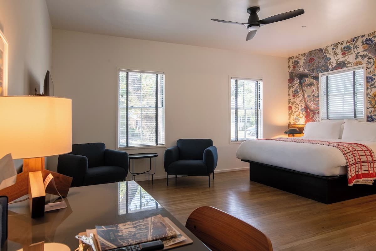 Habitación de hotel con cama, dos sillas, una mesa y un ventilador de techo.