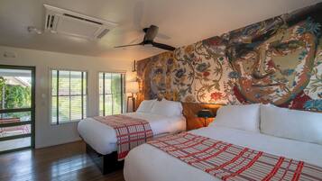 A hotel room with two beds, a ceiling fan, a large floral mural, and a view of the outdoors through the windows.
