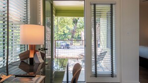 A room with a desk, a lamp, and a view through a glass door to an outdoor area with a patio and a car parked outside. - Talbot Commons Hotel (Taylor)