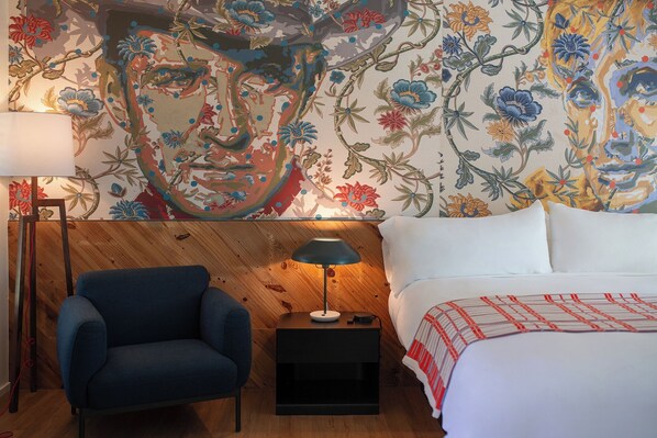 A room with a wooden headboard, a blue armchair, a bedside table with a lamp, and a bed with a white and red striped blanket.