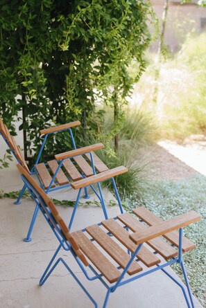 A row of wooden benches with blue metal frames, positioned on a concrete surface with a grassy area and a tree in the background.