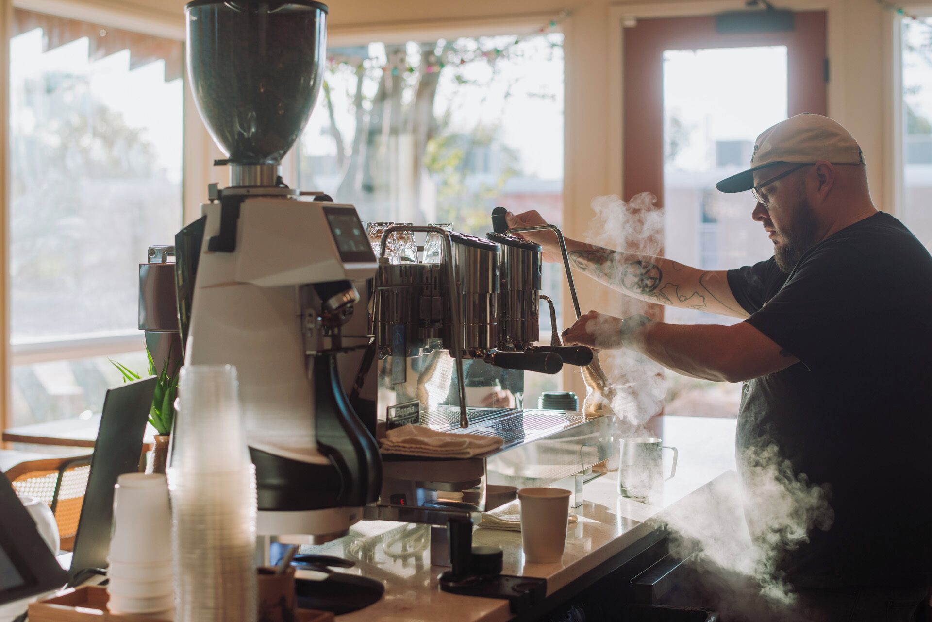 A person operating a coffee machine in a cafe with a window view.