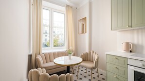 Une cuisine moderne avec une table ronde, deux chaises, une machine à café et une vue sur les immeubles par la fenêtre.