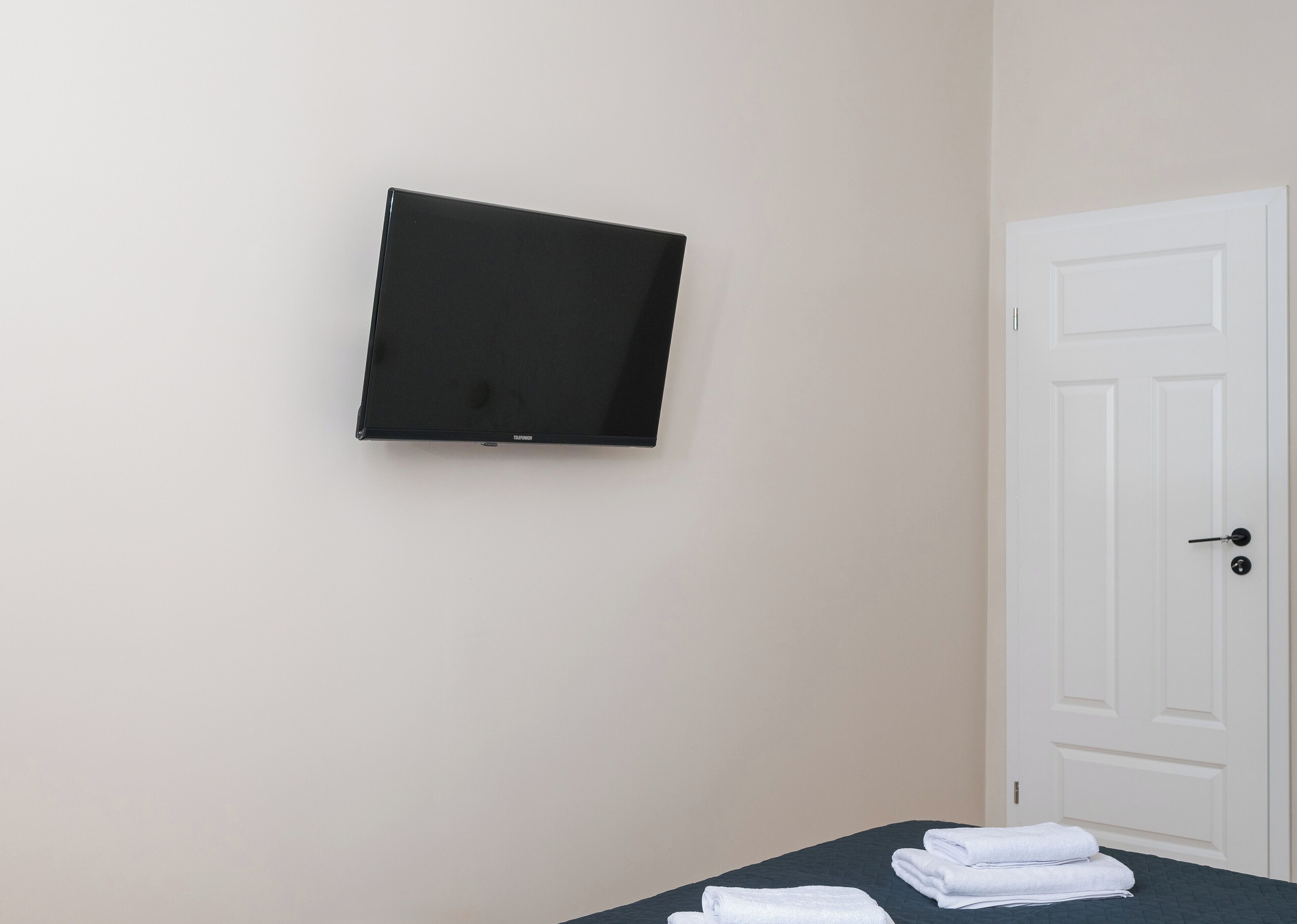 A room with a bed, a flat-screen TV mounted on the wall, and a white door.