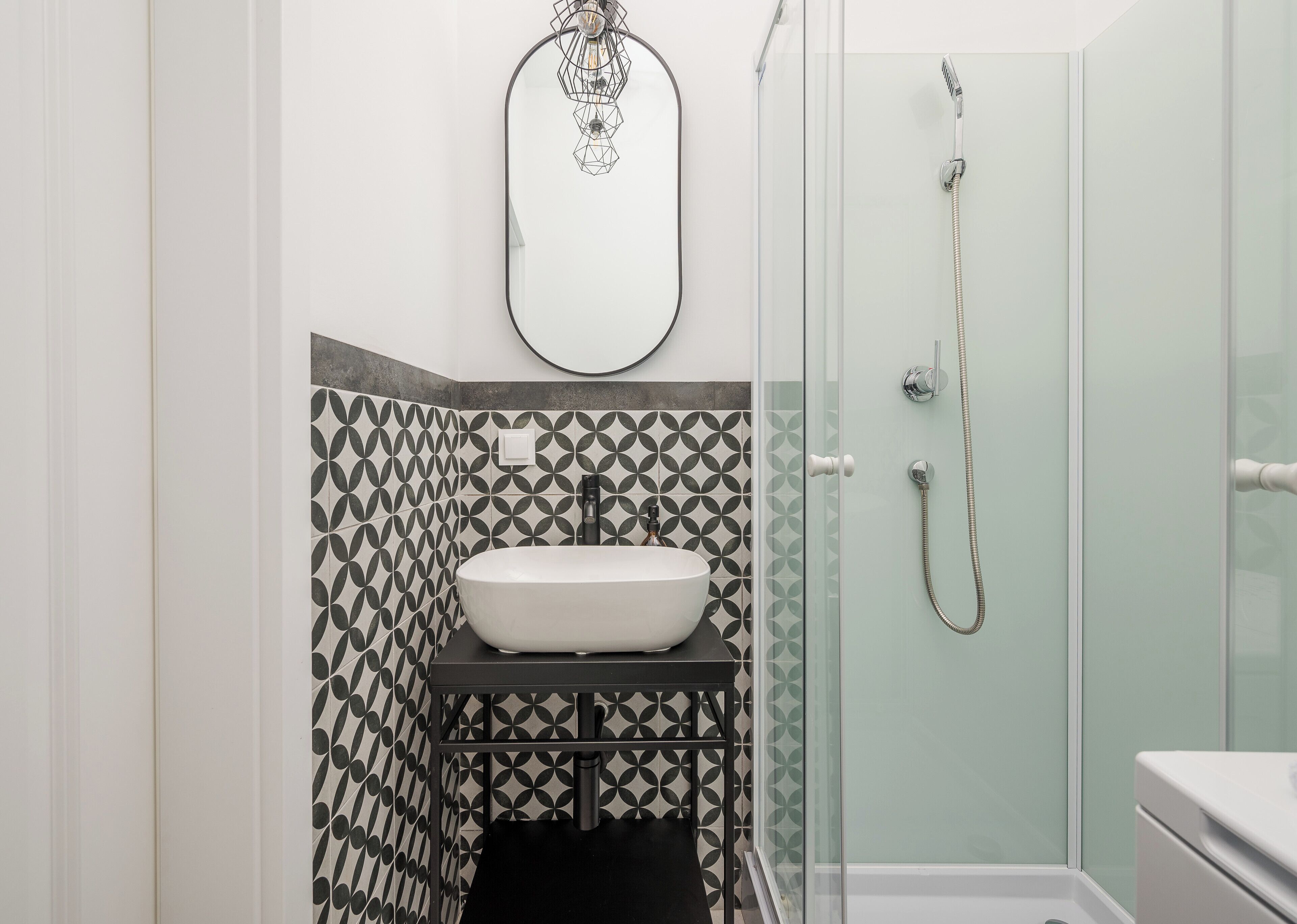 A bathroom with a white sink, a glass shower enclosure, and patterned tiles.