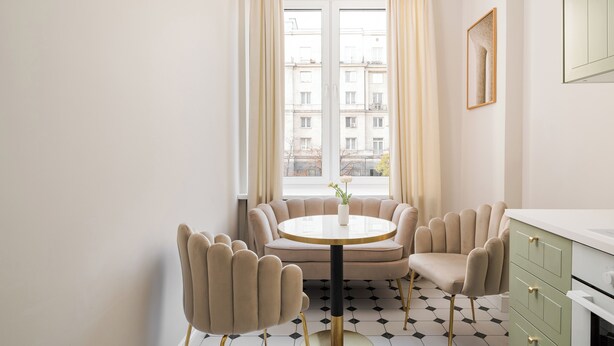 Un espace de salle à manger moderne, avec une table ronde, des chaises rembourrées et une vue sur les bâtiments grâce à de grandes fenêtres.