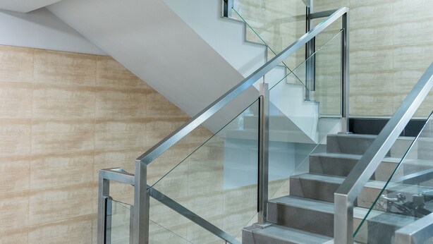 Uma escadaria moderna com guarda-corpos de vidro e parede revestida de azulejos bege.