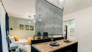 Quarto de hotel moderno com uma cama, um sofá pequeno, uma mesa de jantar com dois banquetes e uma cozinha.