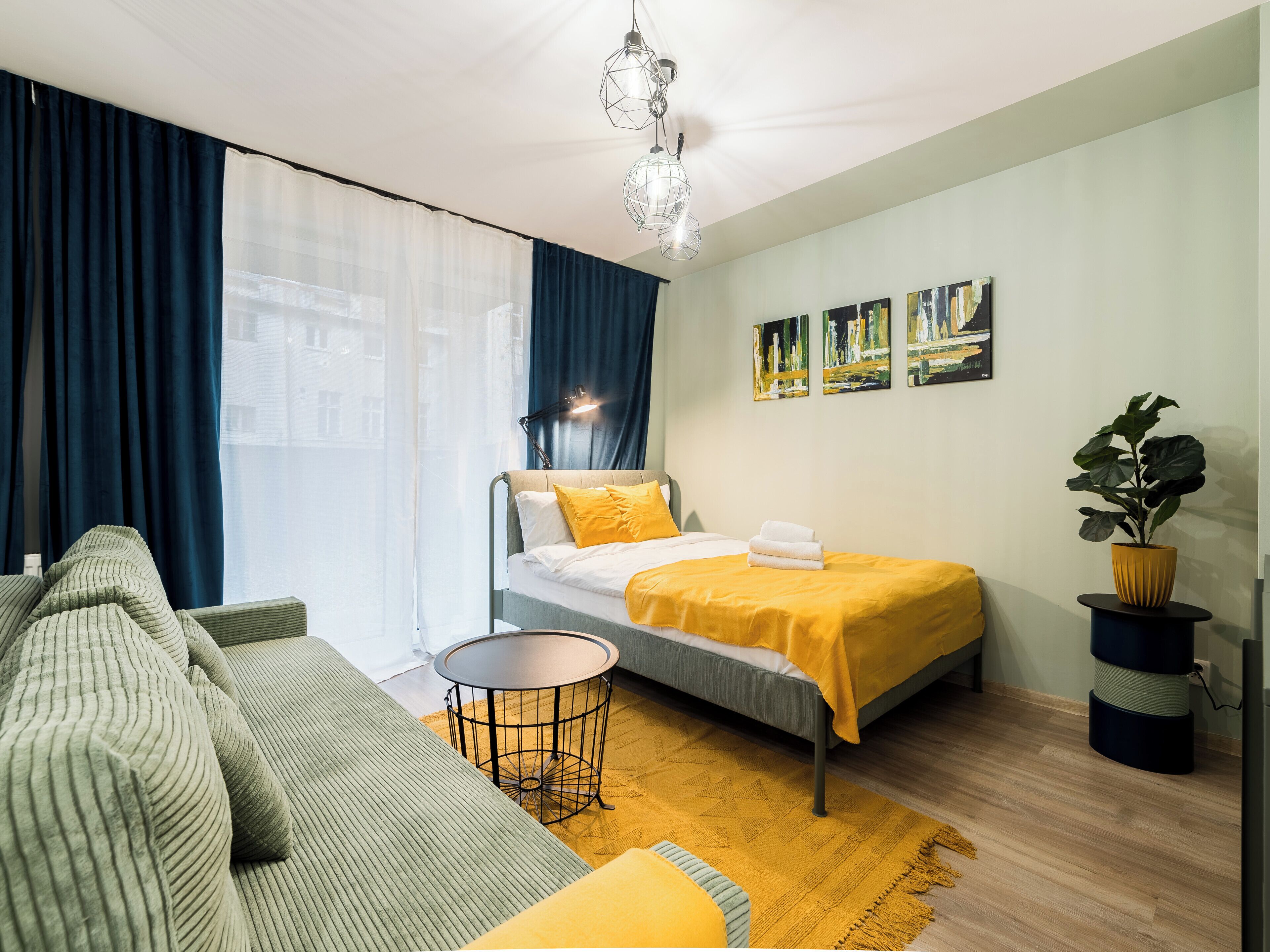 Een moderne hotelkamer met een bed, een bank, een klein rond tafeltje en een potplant.
