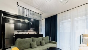 Uma sala moderna com um sofá verde, uma mesa de centro preta e uma cama com roupa de cama amarela.