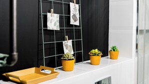Casa de banho com bancada branca, um varal de metal com prendedores de roupa segurando toalhas brancas e três plantas em vasos amarelos.