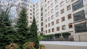 Un edificio residencial de varios pisos con fachada uniforme, ventanas amplias y un área arbolada y con arbustos.