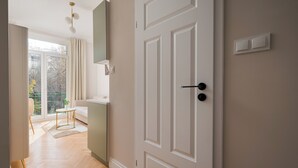 A modern interior with a wooden floor, a white door, and a view through a large window to an outdoor balcony. - Urban Heart Deluxe Studio #2 (Warszawa)
