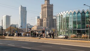A cityscape with a prominent historic building, modern skyscrapers, and a tram stop with people waiting. - Urban Heart Deluxe Studio #2 (Warszawa)