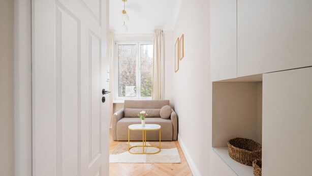A hallway with a beige sofa, a small round table with a vase, and a white door. - Urban Heart Deluxe Studio #1 (Warszawa)