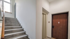 A staircase leading to a door with a number plate, a doormat, and a window with a view of trees. - Urban Heart Deluxe Studio #1 (Warszawa)