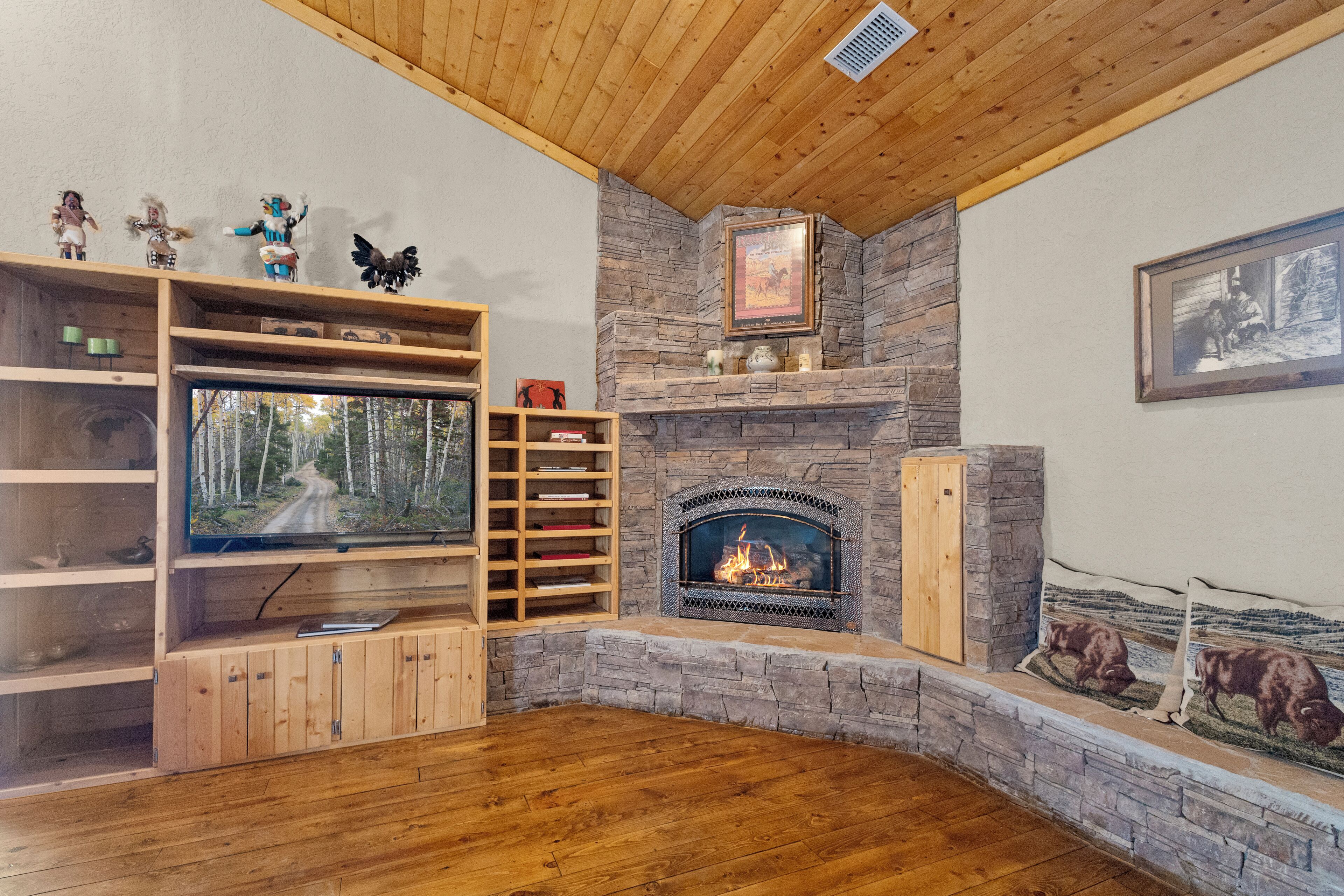A cozy living room with a stone fireplace, wooden shelves, and a television.