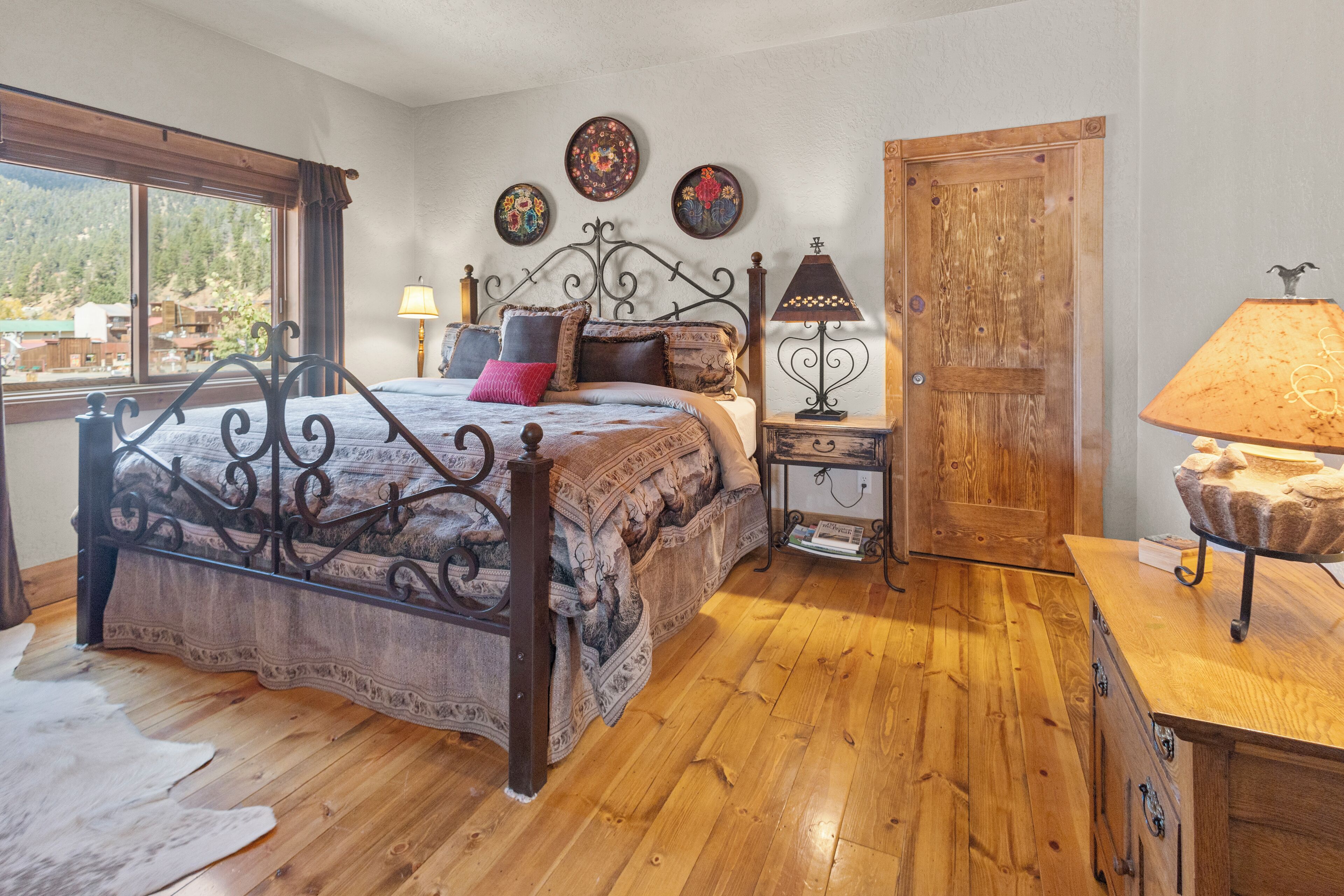 Een slaapkamer met een houten bed, een nachtkastje met een lamp, een houten dressoir en een raam met uitzicht.
