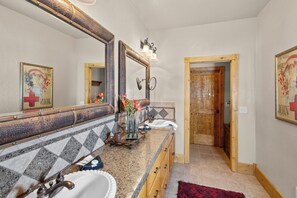 A bathroom with a granite countertop, two sinks, a large mirror, and a wooden door.