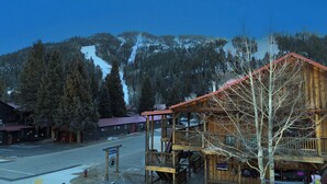 A wooden cabin with a balcony, surrounded by trees and a mountain backdrop.