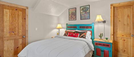 Une chambre à coucher comprenant un lit, une armoire en bois, des tables de chevet et un ventilateur de plafond.