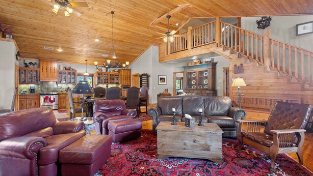 A spacious living area with leather furniture, a wooden staircase, and a kitchen in the background.