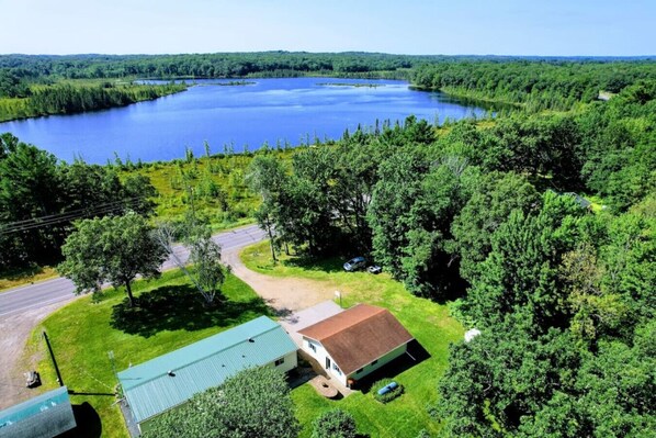 A house with a green roof, surrounded by a forest and a lake.