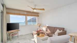 Un salon moderne doté d’un téléviseur à écran plat, d’un canapé, d’une table basse et offrant une vue sur la mer.