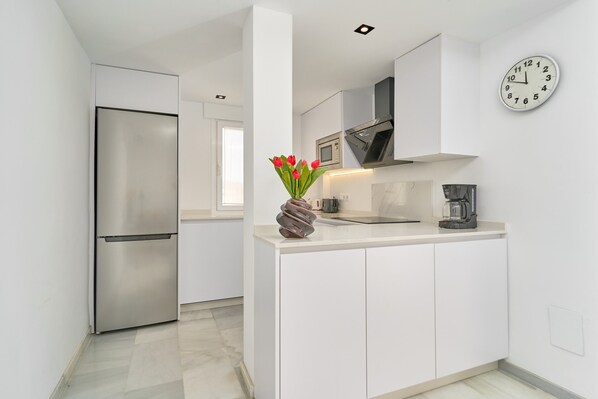 Una cocina moderna con armarios blancos, un refrigerador de acero inoxidable, un microondas y una cafetera.