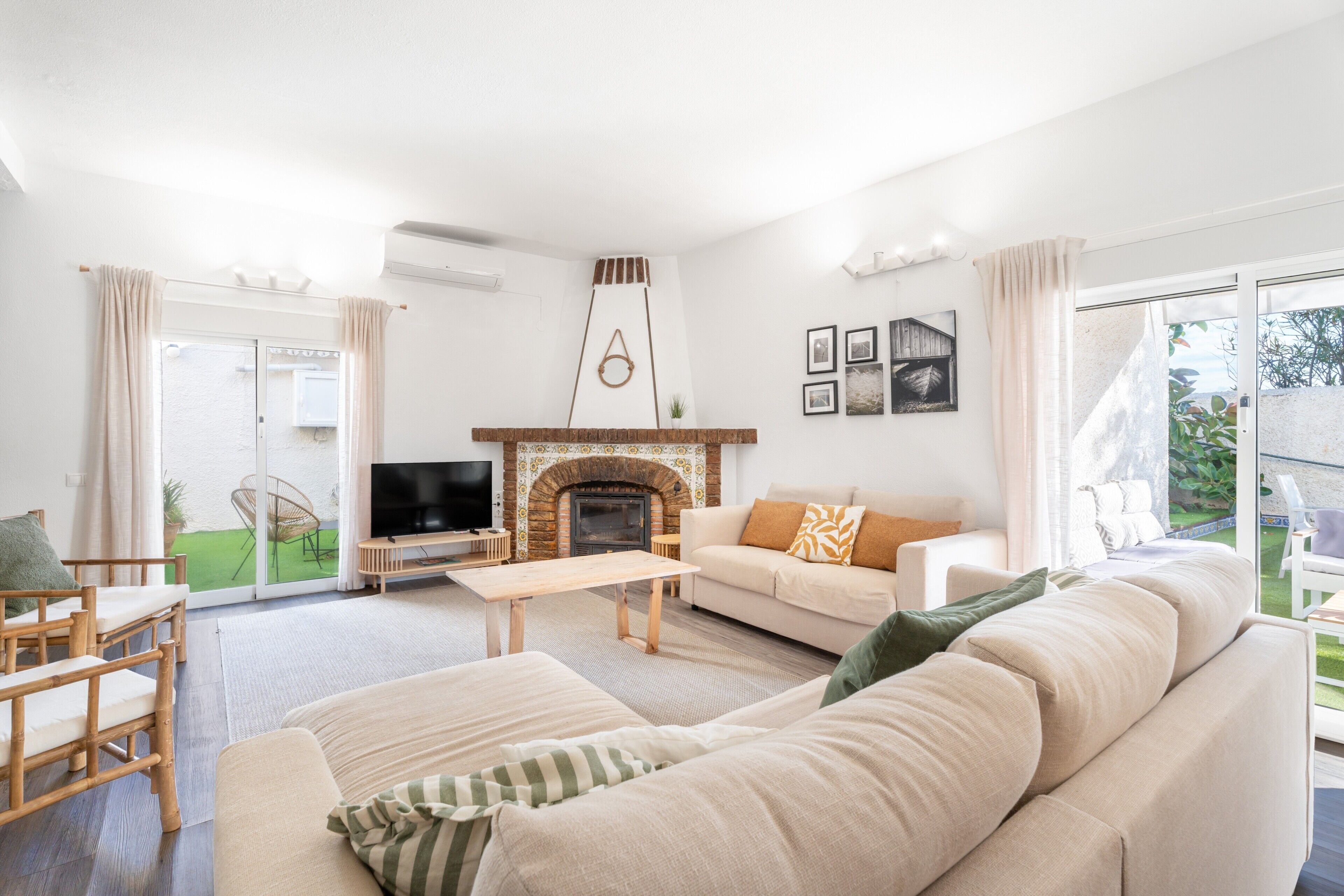 Una sala de estar con chimenea, sofá, televisor y vistas al exterior.