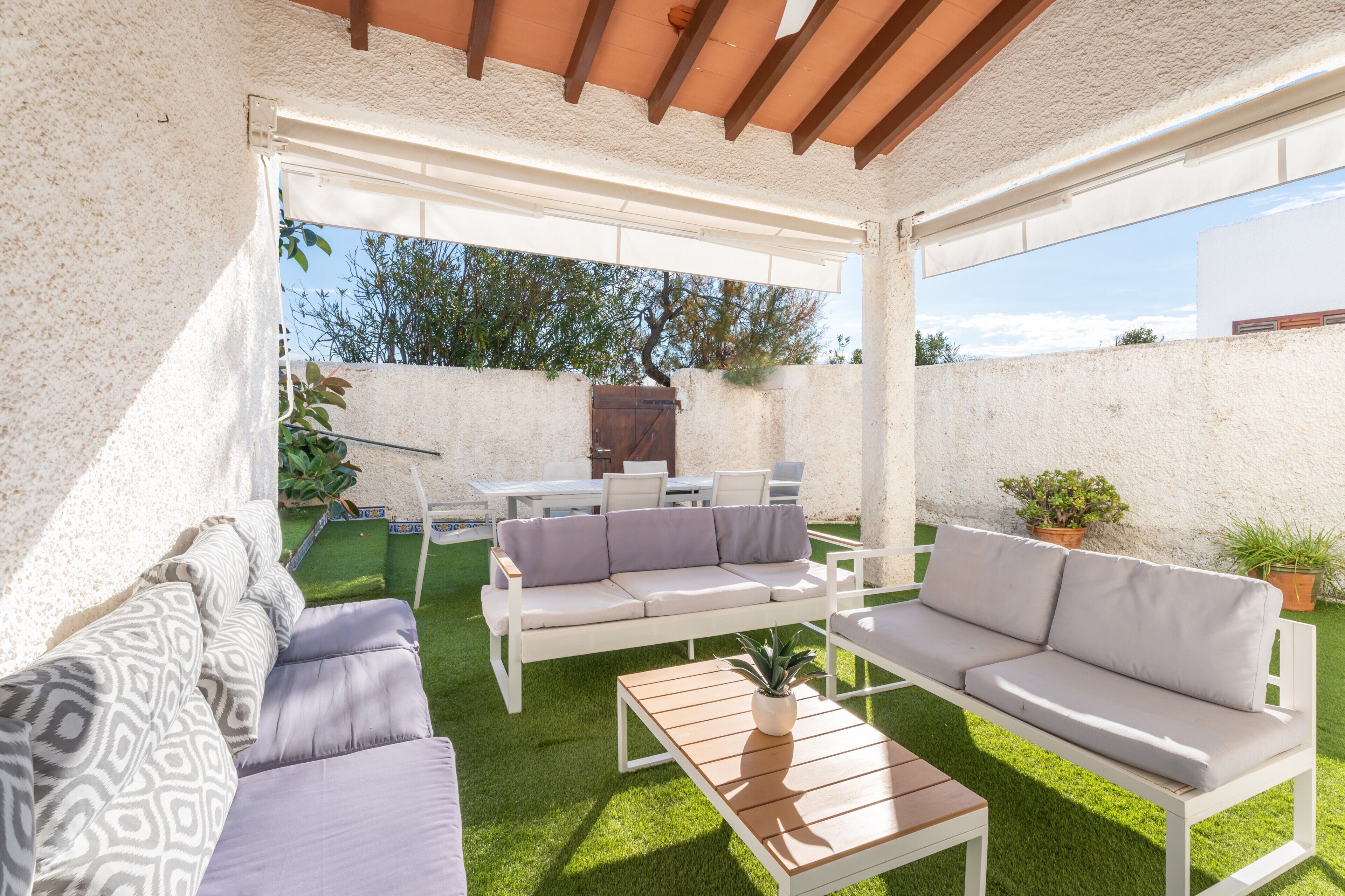 Eine Terrasse mit weißer Möbel, einem Holztisch und einem Blumentopf.