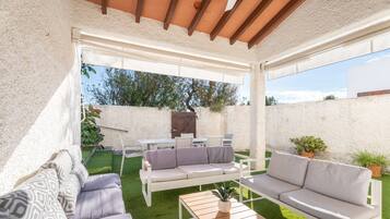 Eine Terrasse mit weißer Möbel, einem Holztisch und einem Blumentopf.