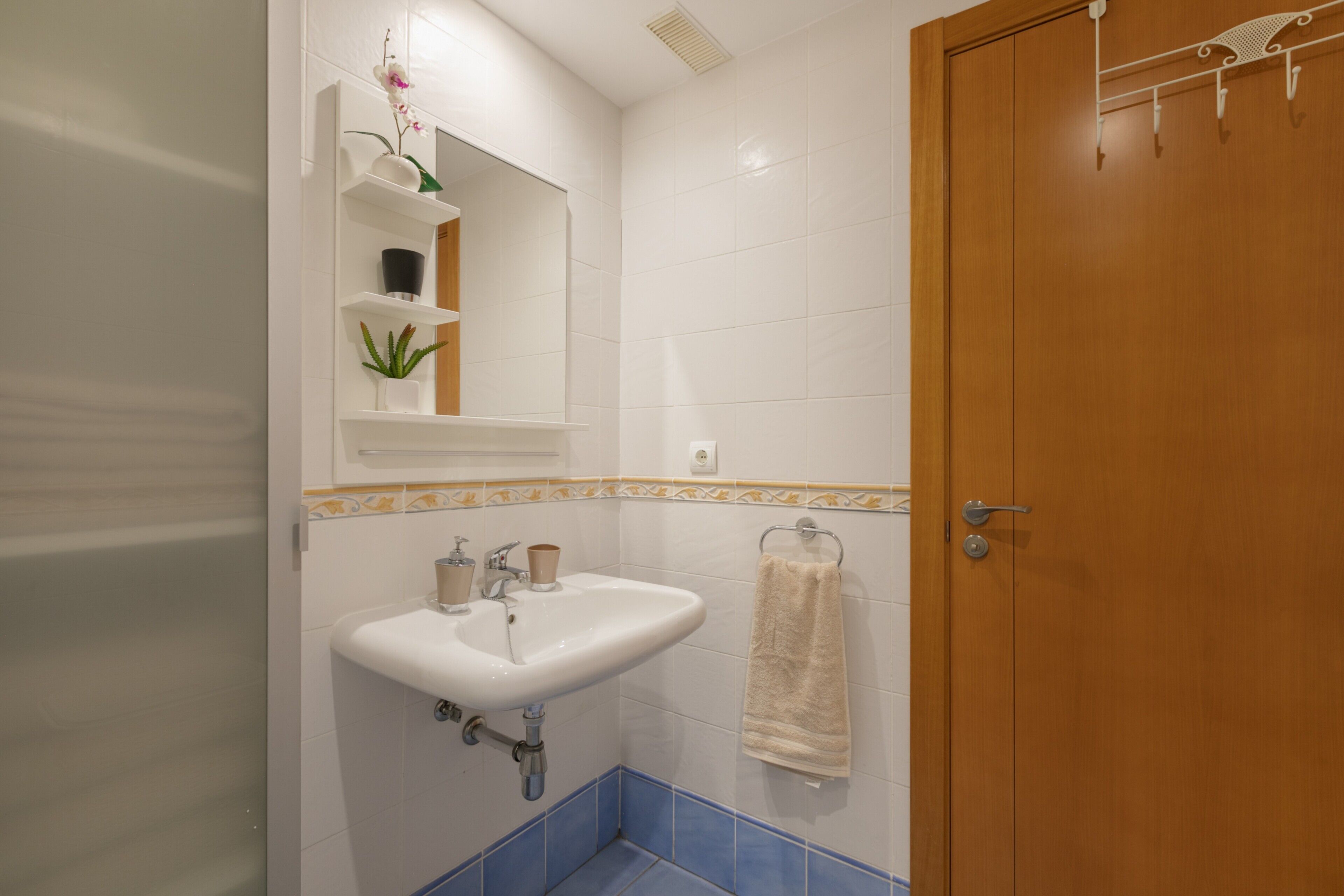 A bathroom with a white sink, a mirror, a towel rack, and a wooden door.