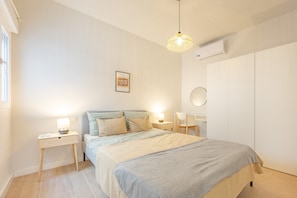 A bedroom with a bed, bedside tables, a lamp, a wall-mounted air conditioner, and a wardrobe.