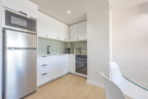 A modern kitchen with a refrigerator, oven, microwave, and a glass table.