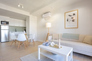 A modern living room with a white sofa, a dining table with chairs, a white coffee table, and a framed artwork on the wall.