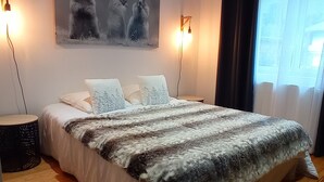 A bedroom with a large bed, two bedside lamps, a painting of bears, wooden flooring, and a window with curtains. - Chalet "Sublime Chalet 14 Pers Spa Extrieur" with Mountain View (Cauterets)