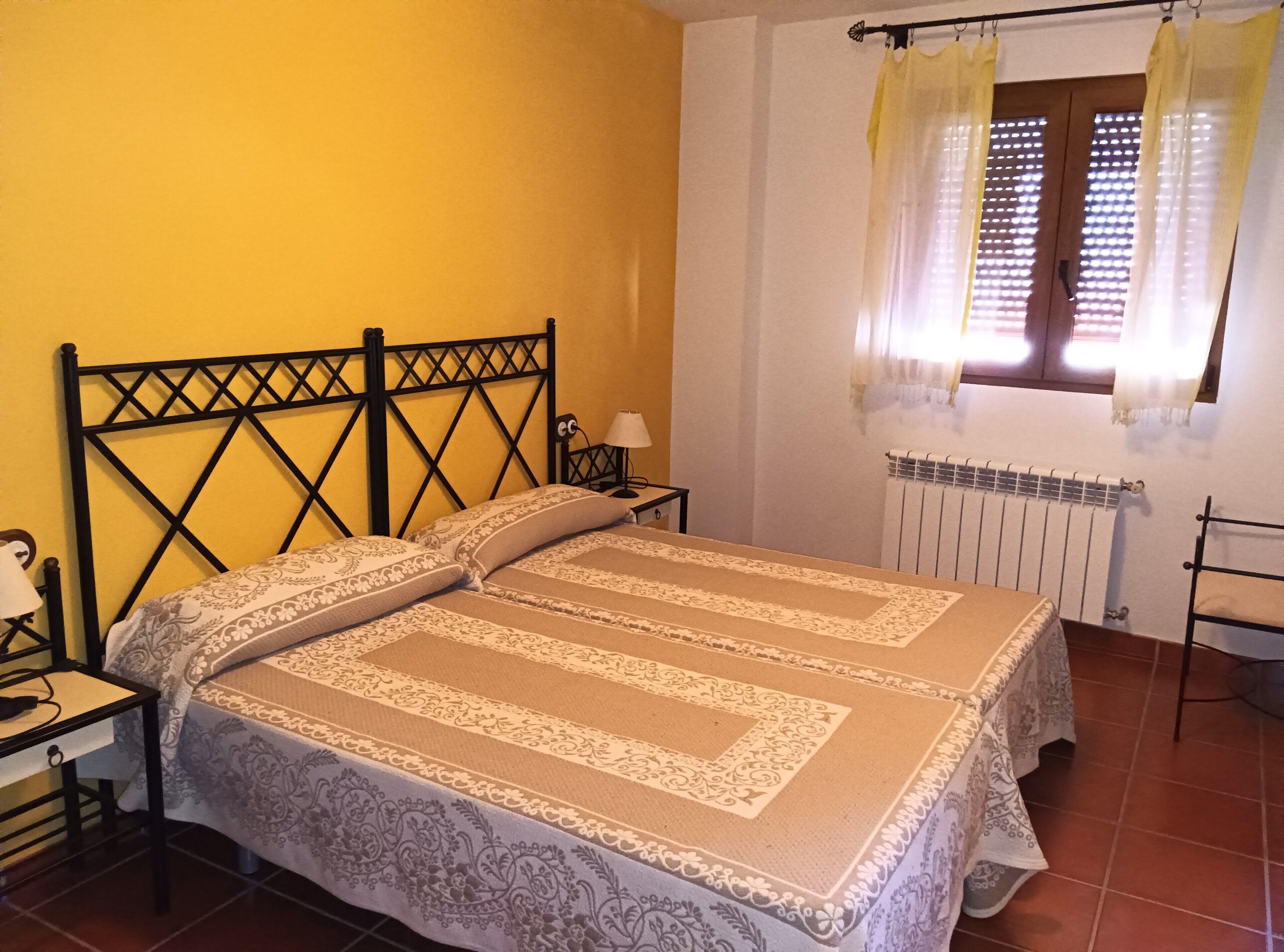 Un dormitorio con una cama, una mesita de noche, una lámpara, una ventana con cortinas y un radiador.