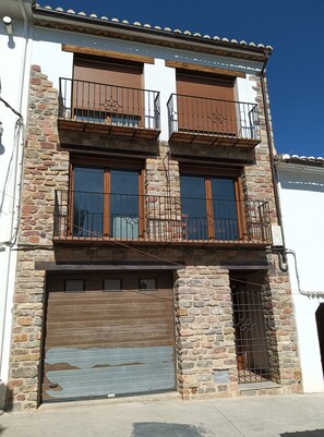 A two-story building with a garage, stone facade, and wooden balconies.