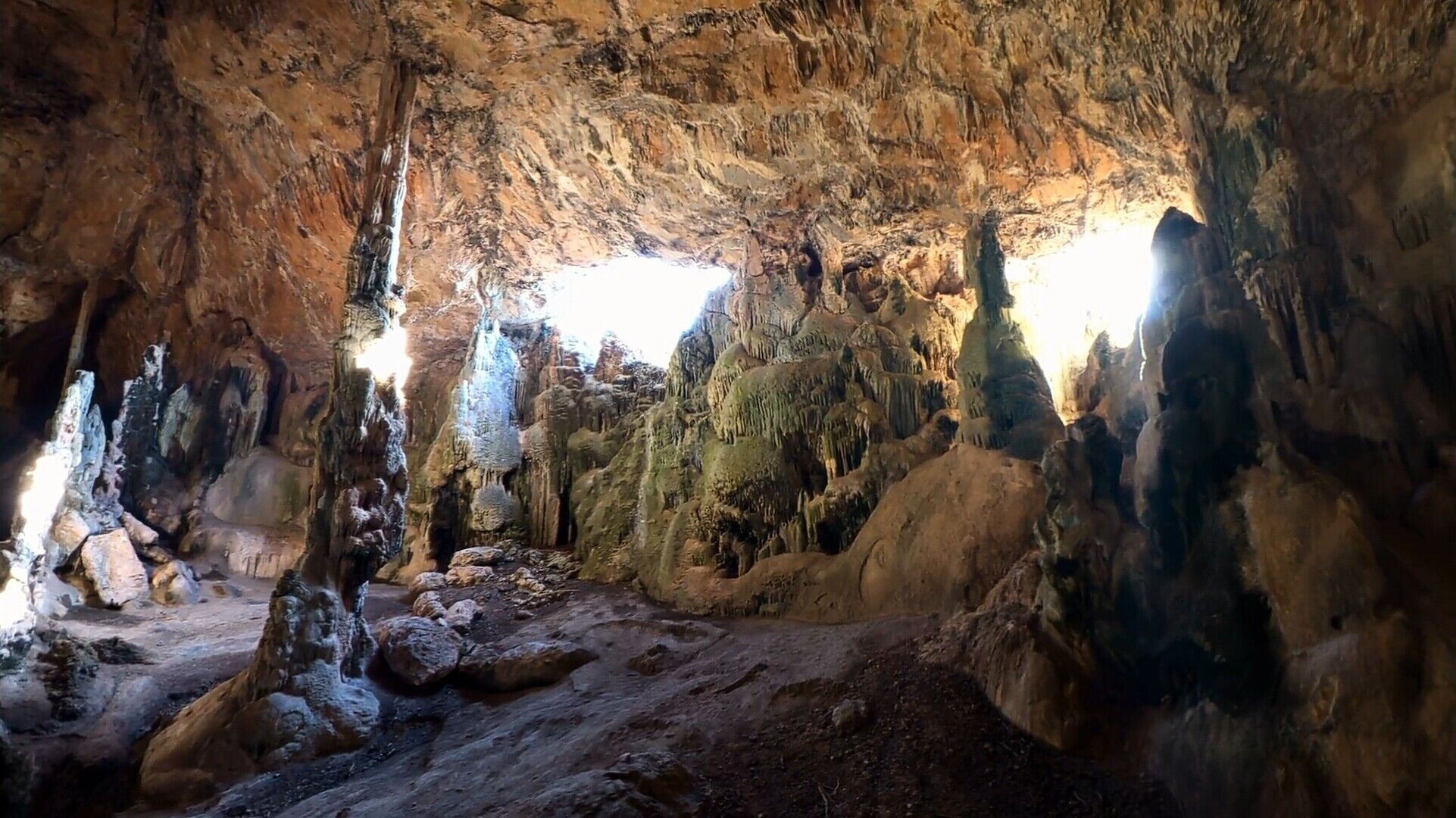 En grotta med stalaktiter och stalagmiter, ojämnt, stenigt underlag och naturligt ljus.