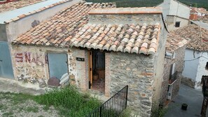 A small stone building with a tiled roof, a visible door, and a staircase leading to the entrance.