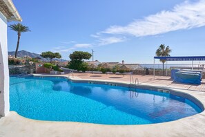 Piscina com água azul cristalina, rodeada por um deck com espreguiçadeiras e área coberta.