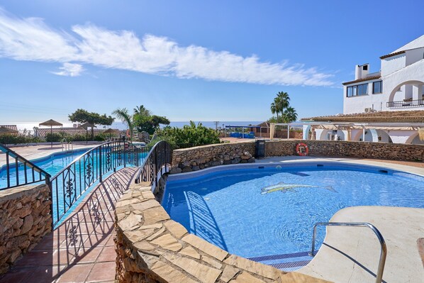 A swimming pool with stone walls and metal railings, surrounded by a stone patio and a view of the sea.